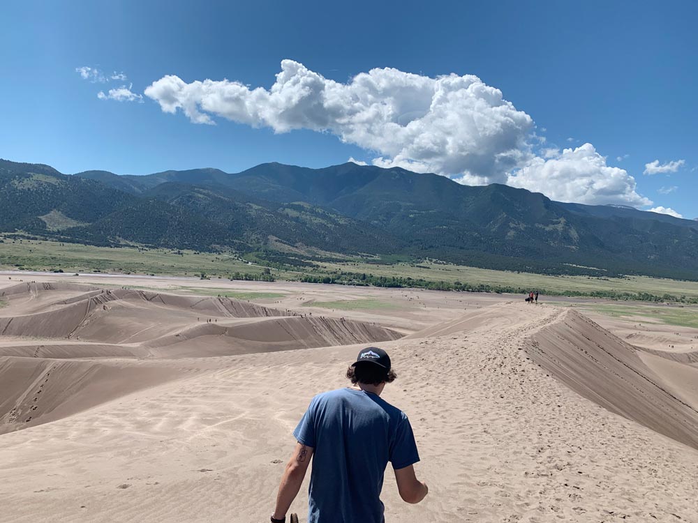 Guy walking on sand dunes with mountains in the distance
