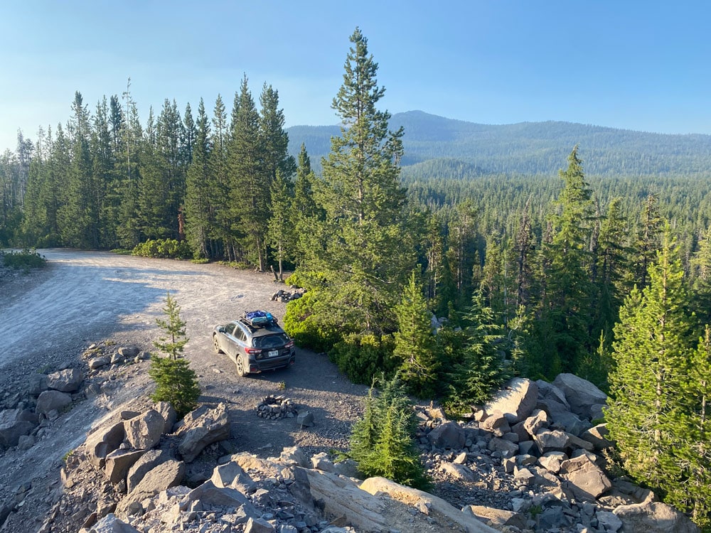 aerial view of a Crosstrek on a dirt mountain road pull out and campground with vast forest beyond