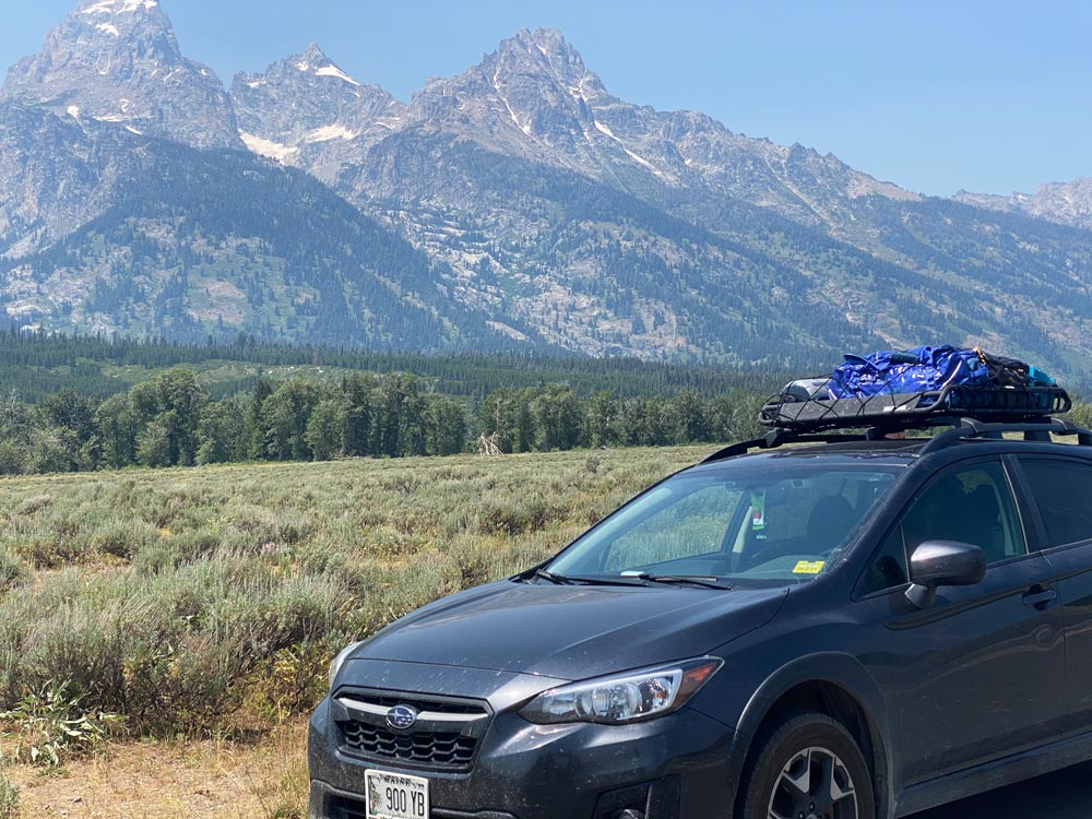 Crosstrek in front of a meadow with a forest in the background and a mountain behind that