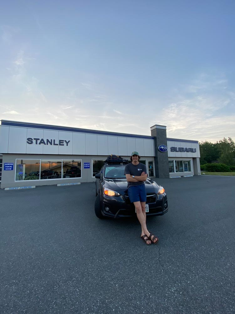 Jack, leaning back onto the hood of his Subaru Crosstrek in front of the Stanley Subaru dealership