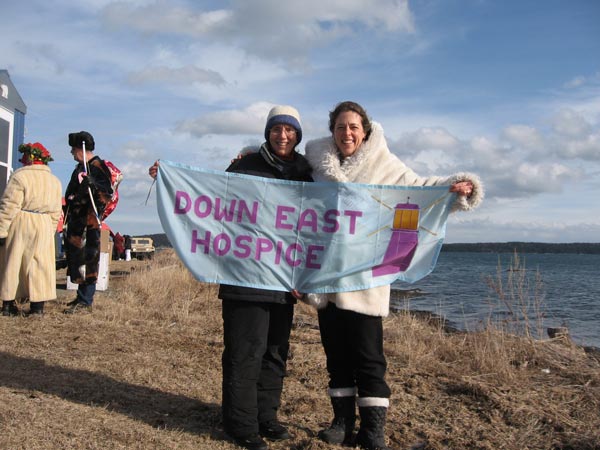 Two Down East Hospice Volunteers hold a DEHV banner in front of the water