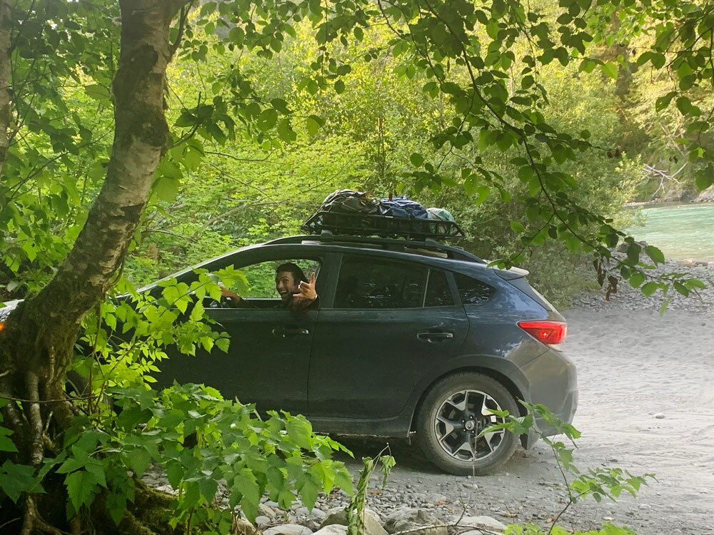 Guy driving a Crosstrek along a dirt path in the middle of a lush green woods