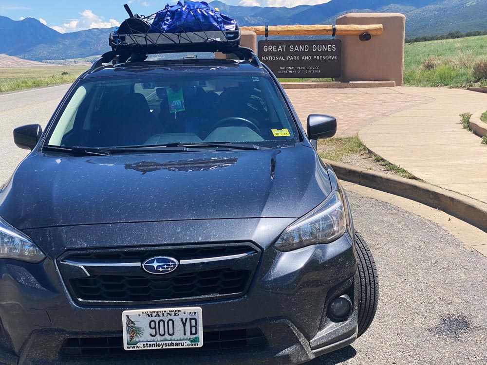 Crosstrek in front of the Great Sand Dunes National Park and Preserve sign with mountains behind