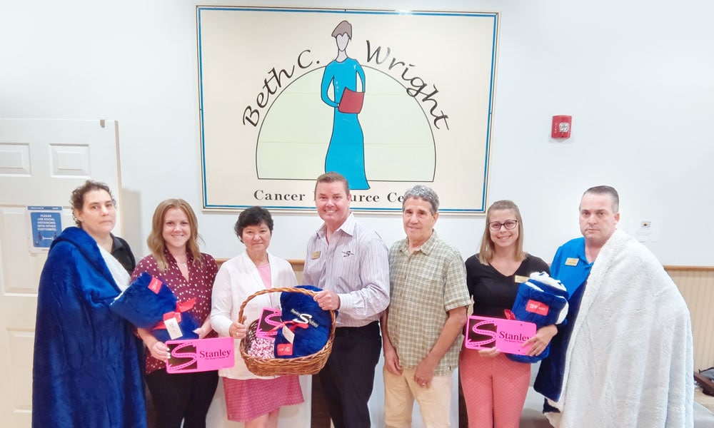 Stanley Subaru team and Beth C Wright Center staff standing with the blankets, the Hershey Kisses, and pink Stanley license plates in front of the mounted Beth C Wright Cancer Resource Center sign