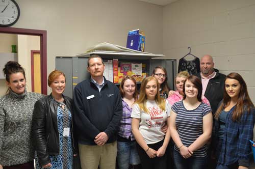 Educators, students, and Stanley Subaru staff pose in front of one of the cabinets full of food at Ellsworth High School