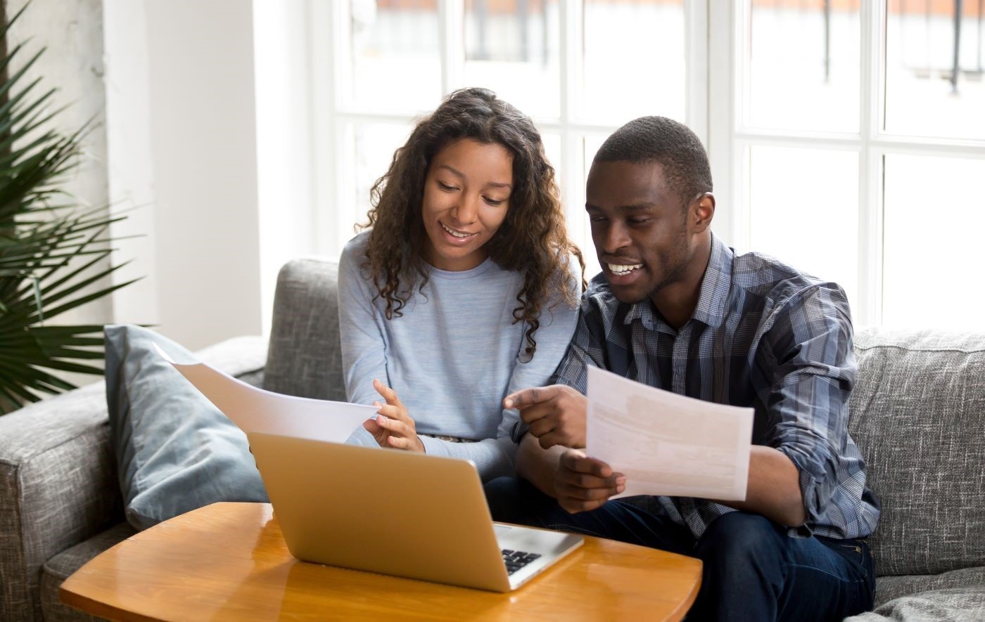 couple on couch looking over online financing on laptop and paperwork