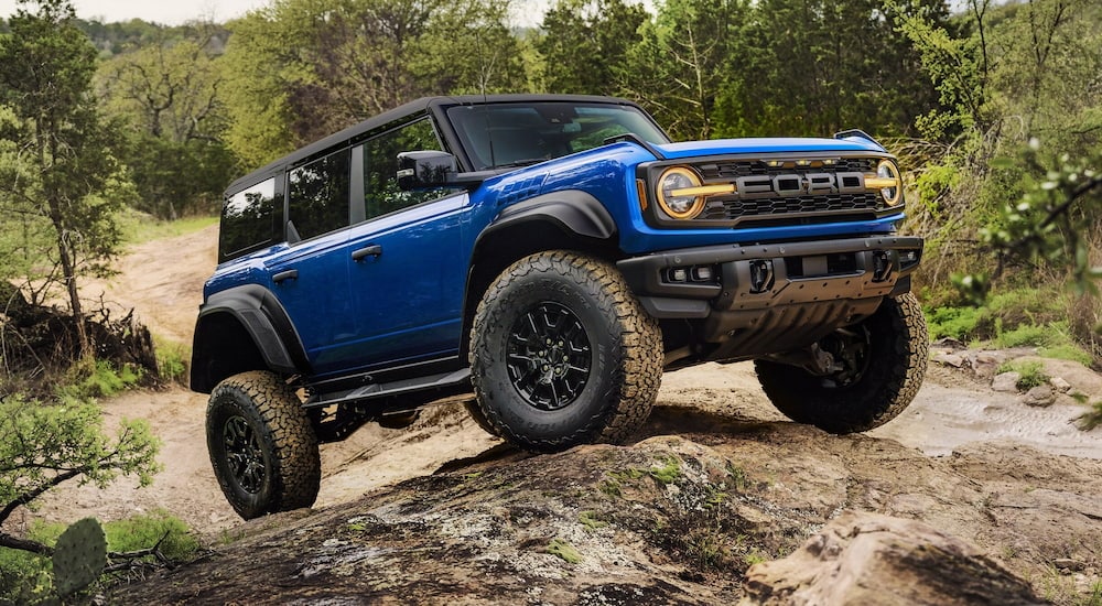 A blue 2025 Ford Bronco Raptor off-roading over large boulders.