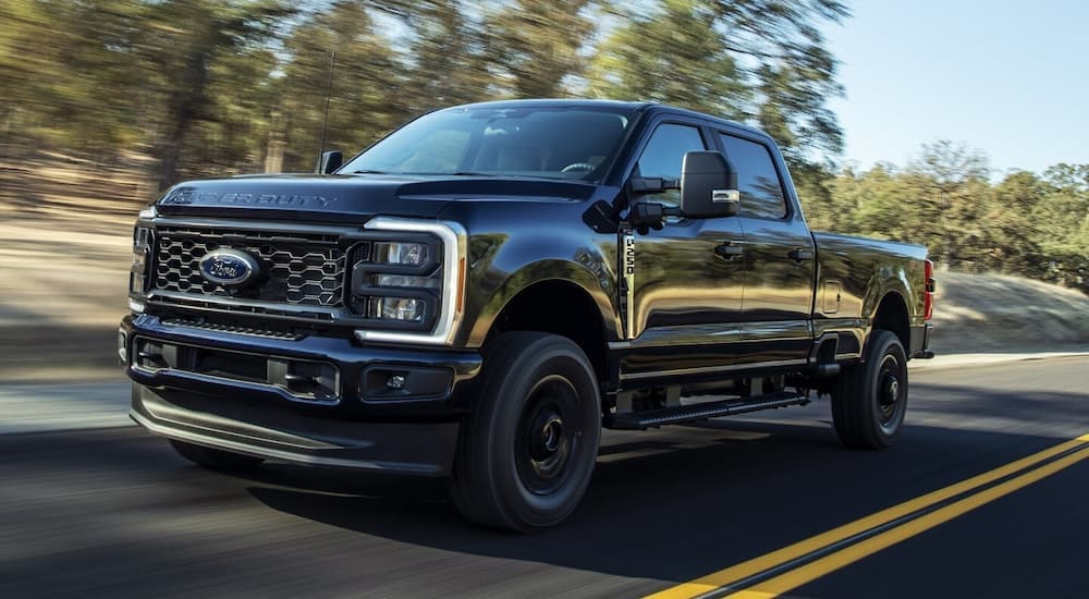 A black 2024 Ford F-250 Super Duty STX is driving on an open road.