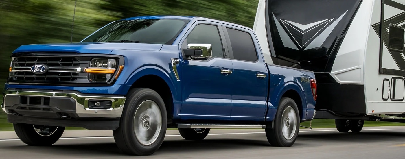A blue 2024 Ford F-150 towing a large camper.