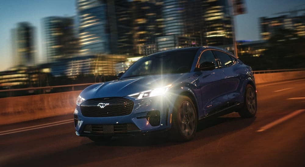 A blue 2024 Ford Mustang Mach-E GT is driving on a city highway at night.