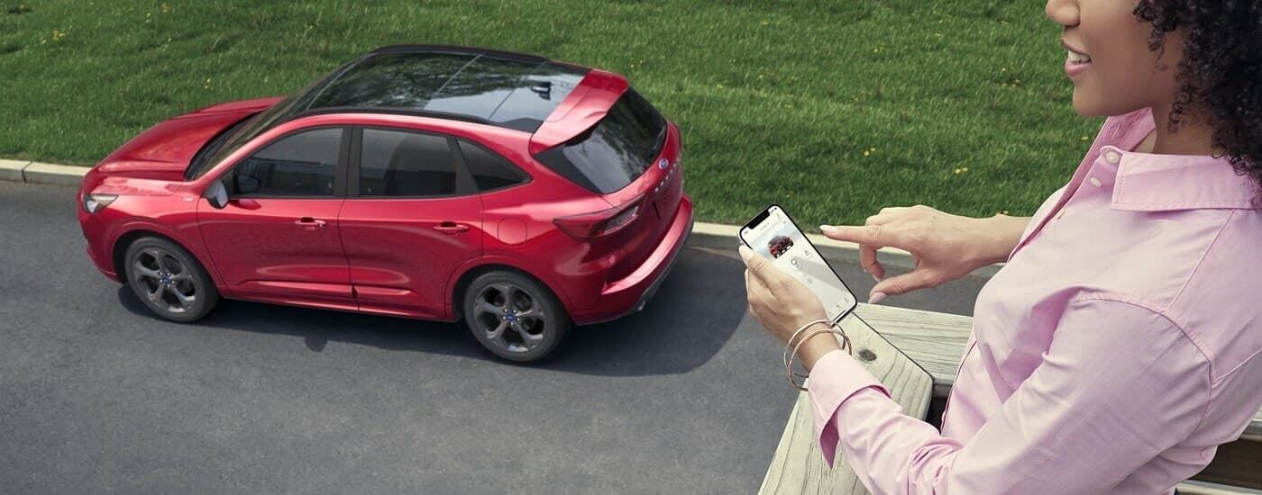 High rear angle view of a red 2024 Ford Escape parked by a curb while a woman uses her phone.