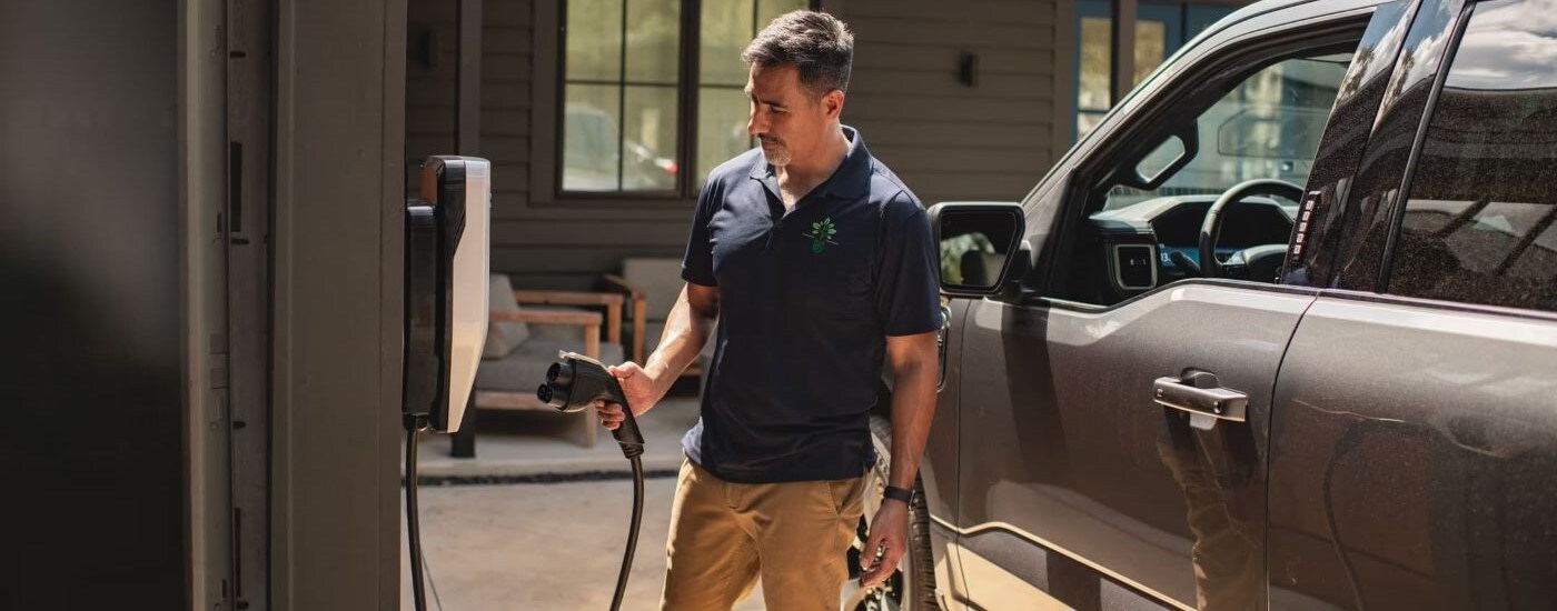 Man plugging in a grey 2023 Ford F-150 Lightning to a charging port.
