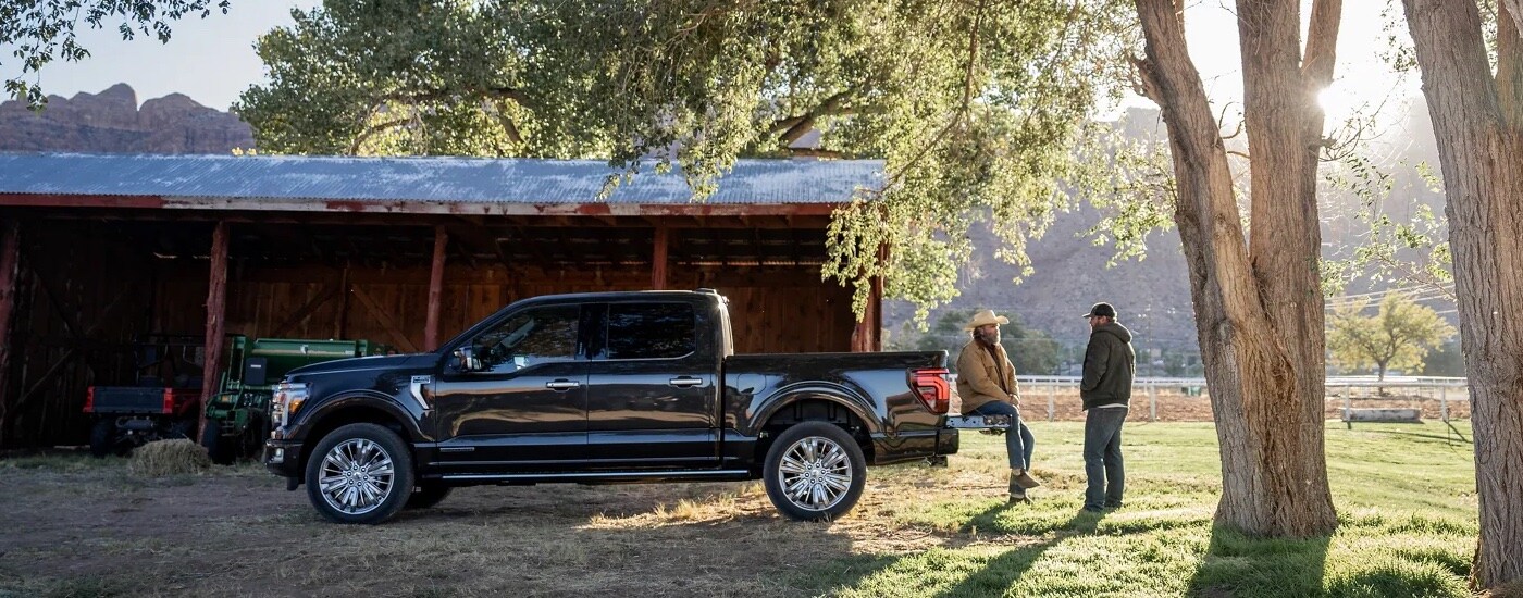 A black 2024 Ford F-150 parked near trees and a shed on a farm.