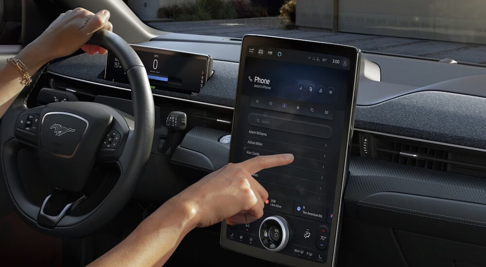 A driver using the infotainment screen in a 2024 Ford Mustang Mach-E for sale near Jackson.