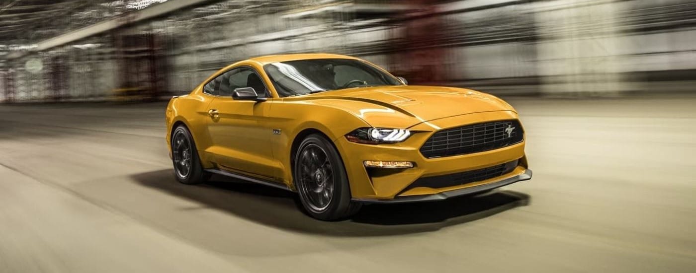 A yellow 2022 Ford Mustang GT driving through a blurred tunnel to a used car dealer.