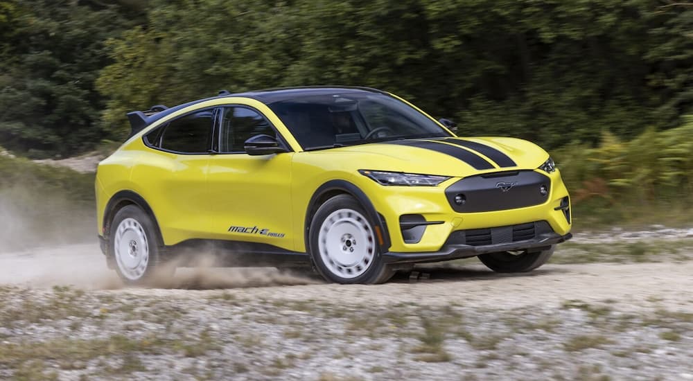 A yellow 2024 Ford Mustang Mach-E Rally is driving on a dirt road.