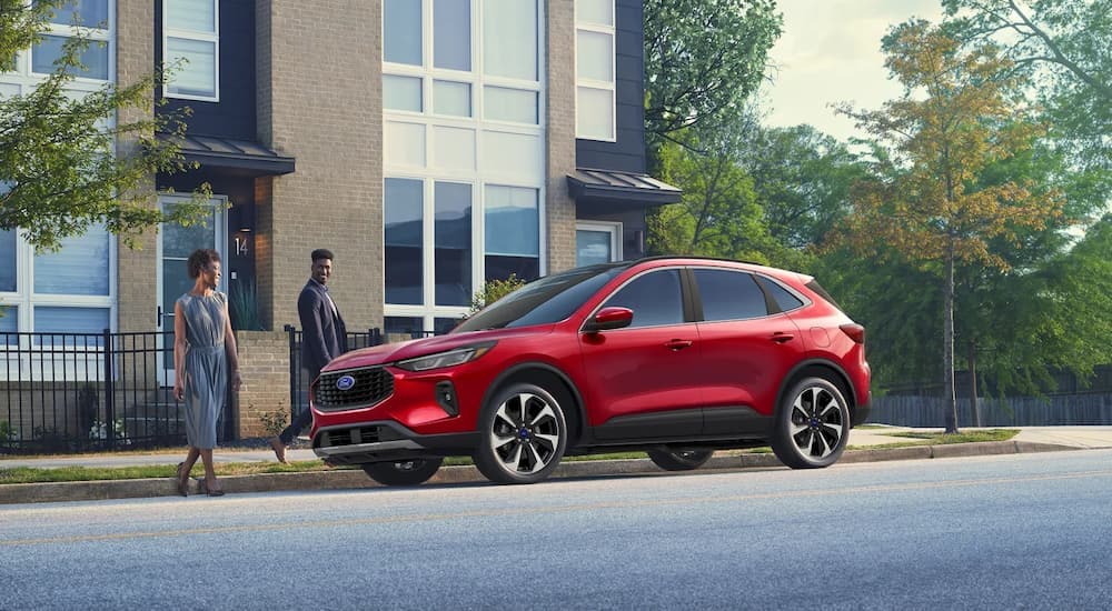 A couple is walking towards a red 2024 Ford Escape parked on the side of a street.