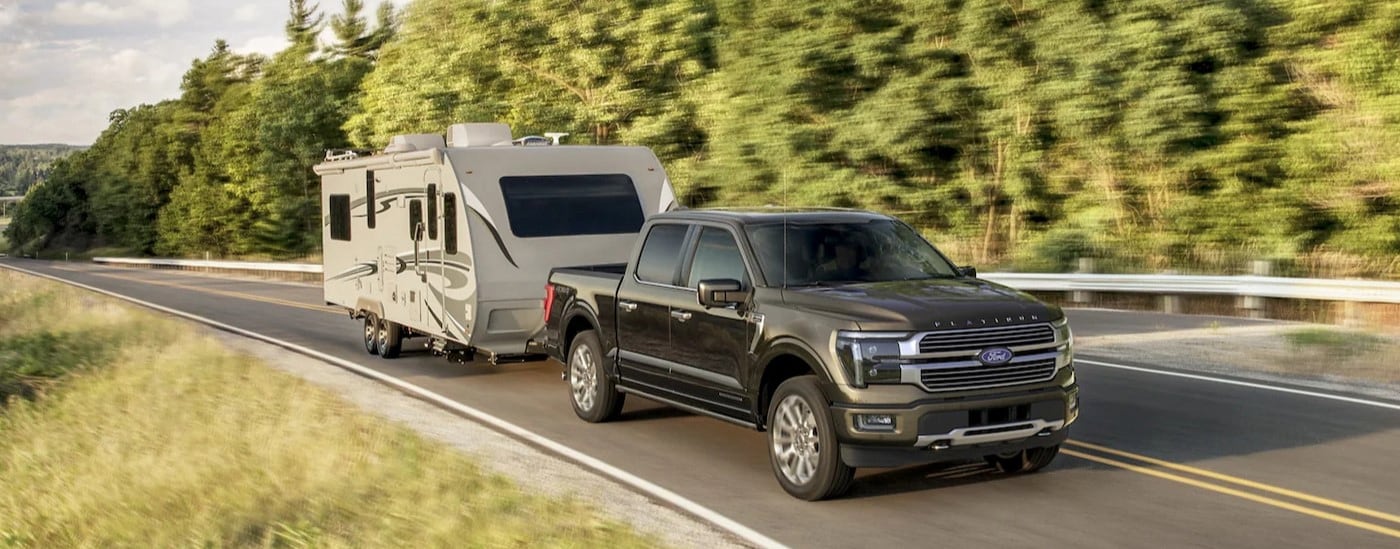 A black 2025 Ford F-150 Platinum Plus is shown towing a trailer on a highway.