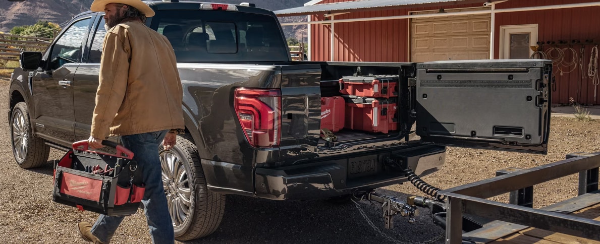 Two people exiting a 2025 Ford F-150® XLT pickup in Rapid Red hitched to a trailer of ATVs