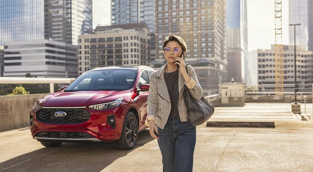 Red 2025 Ford Escape parked in a city as a woman walks by.