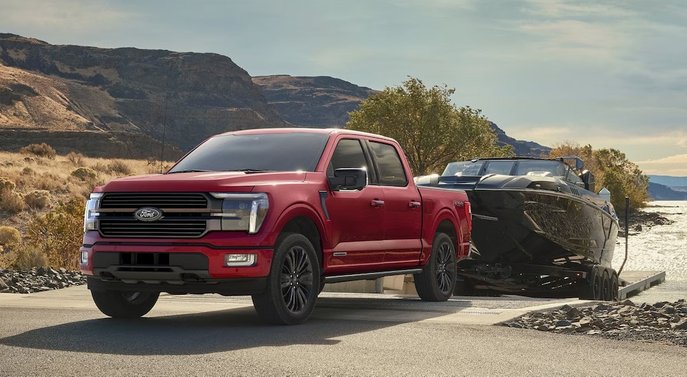 A red 2025 Ford F-150 Platinum towing a boat at a lake.