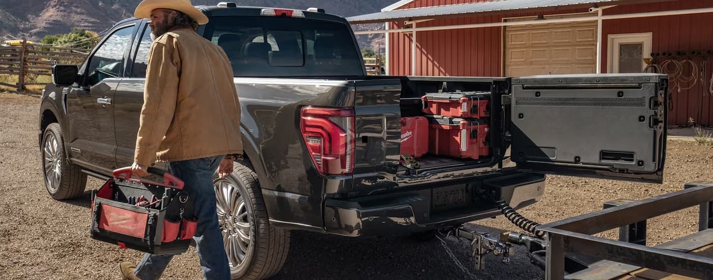 A farm worker is walking past a grey 2024 Ford F-150 parked near a barn.