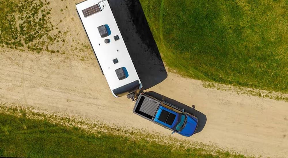 Blue 2025 Ford F-150 towing a trailer on a dirt road.