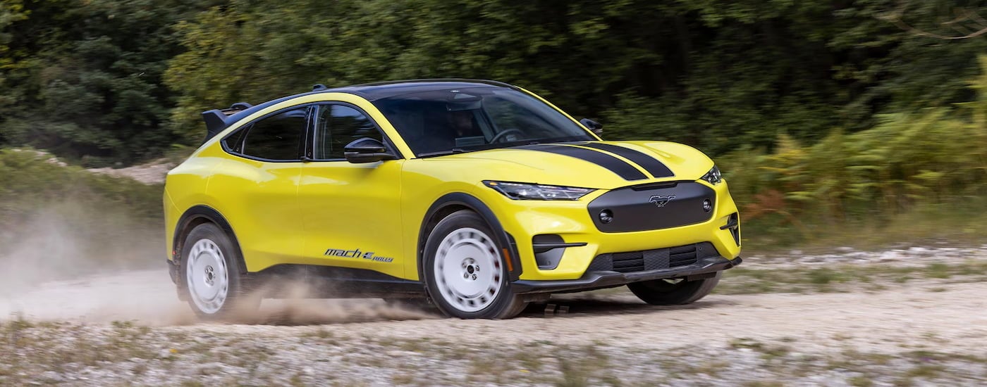 A yellow 2024 Ford Mustang Mach-E Rally Edition driving on a dusty track.