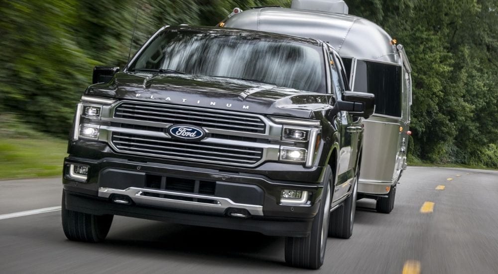 Black 2025 Ford F-150 towing a silver camper.