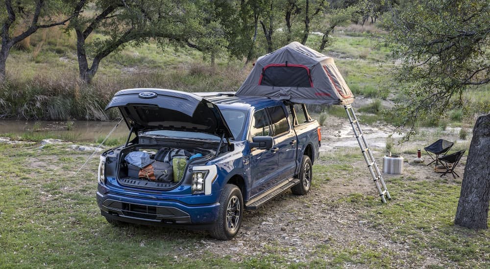 A blue 2024 F-150 Lightning is shown from the front while camping.