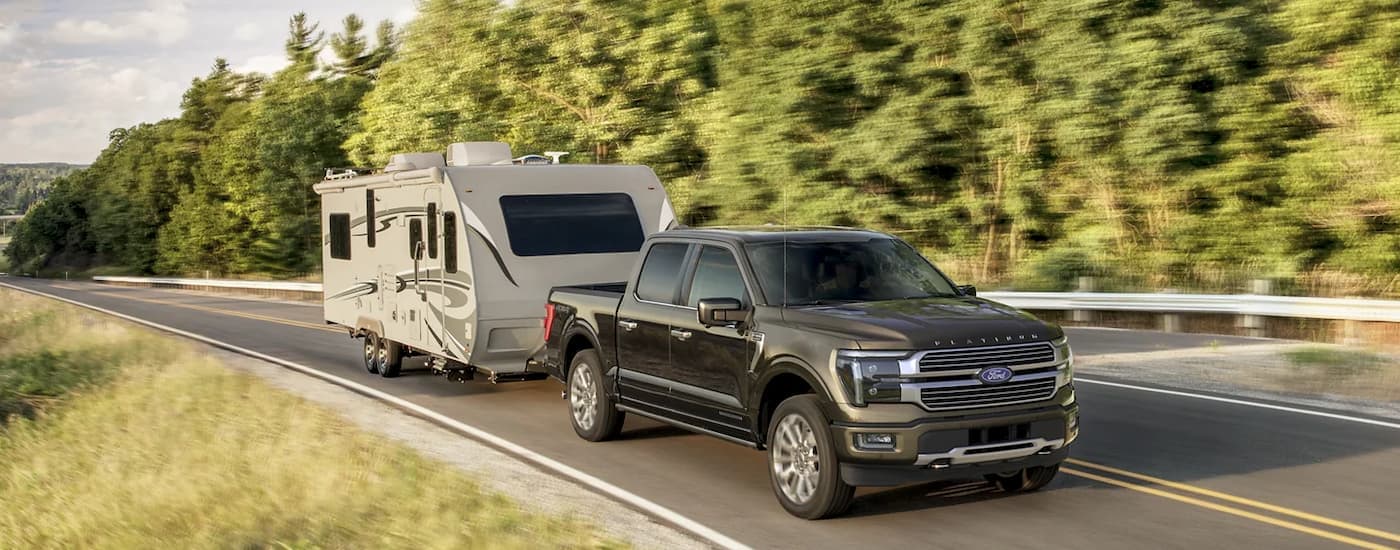 A grey 2025 Ford F-150 towing a camper trailer.