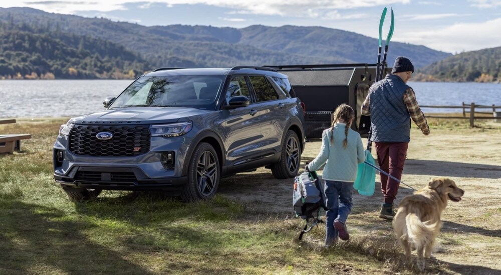 A blue-grey 2025 Ford Explorer ST parked at a lake with a family.