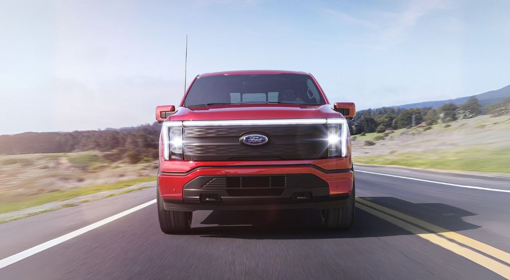 A red 2023 Ford F-150 Lightning for sale is shown driving on an open road.