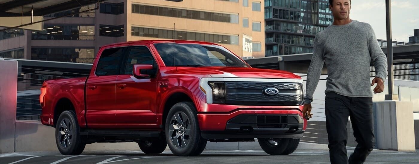 A man walking from a red 2024 Ford F-150 Lightning parked and angled right.