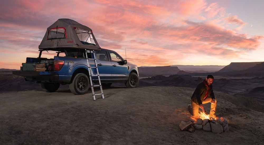 A blue 2025 Ford F-150 parked at a campsite with a tent set up in the bed.