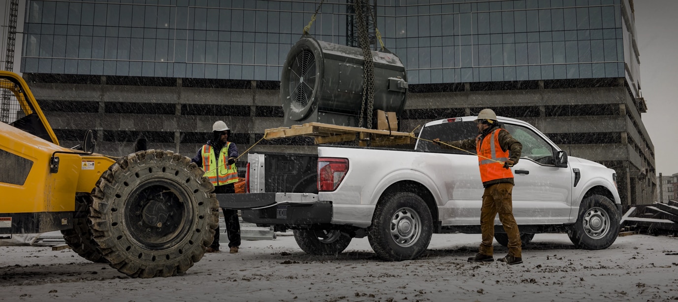 Two people exiting a 2025 Ford F-150® XLT pickup in Rapid Red hitched to a trailer of ATVs
