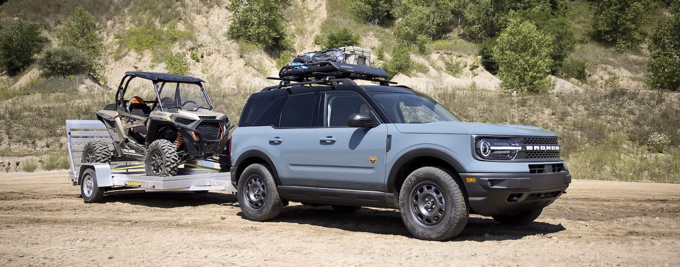 A blue 2023 Ford Bronco Sport Badlands is shown from the side while towing a UTV.