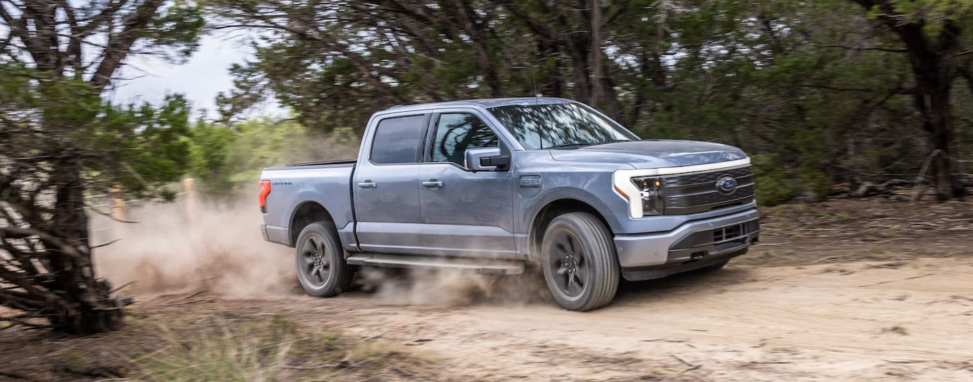 A silver 2024 Ford F-150 Lightning for sale is shown from the side while off-road.