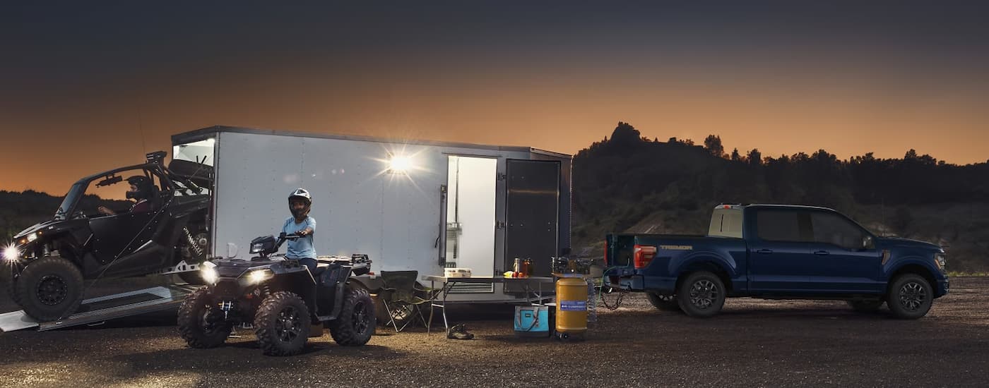 A blue 2025 Ford F-150 Tremor towing a silver trailer for ATVs. href=