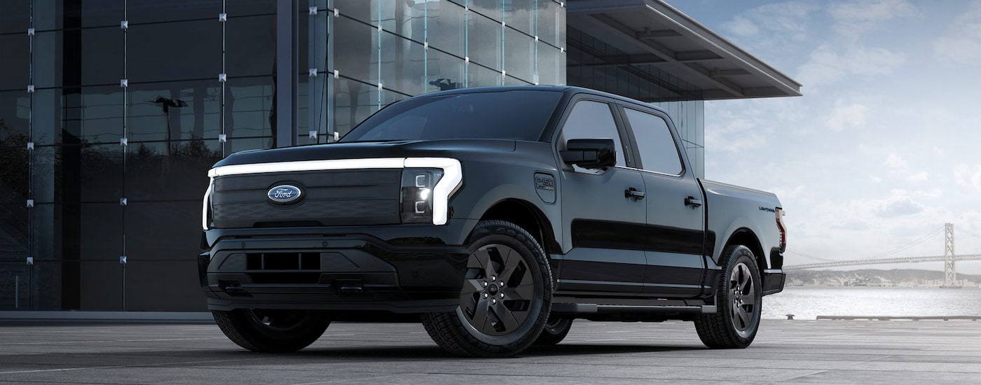 A black 2024 Ford F-150 Lightning Lariat parked outside a glass building.