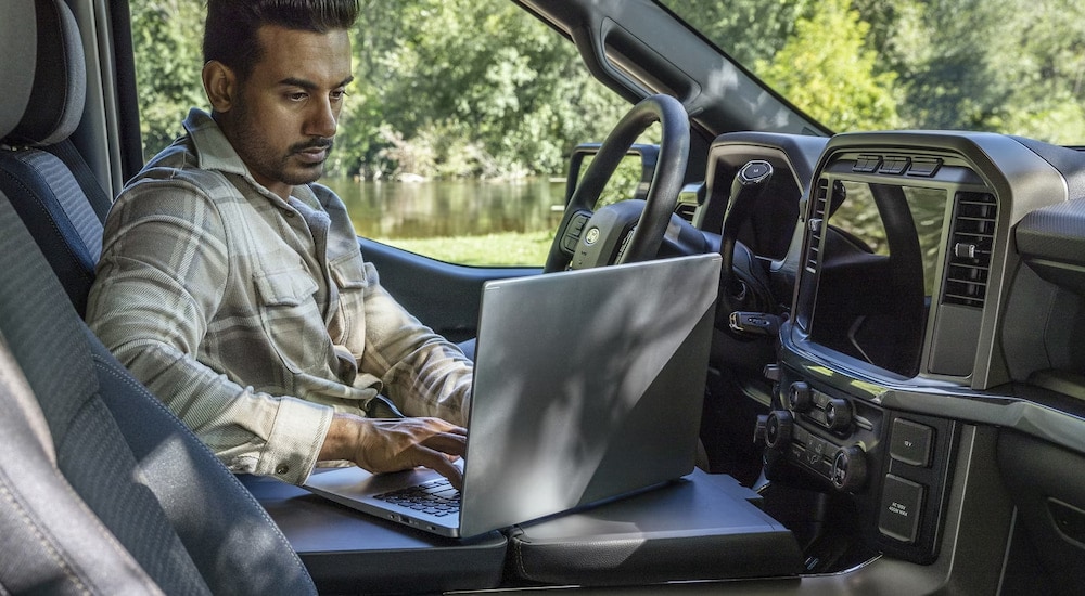 A man using his laptop in the cabin of a 2025 Ford F-150 for sale in Milan.