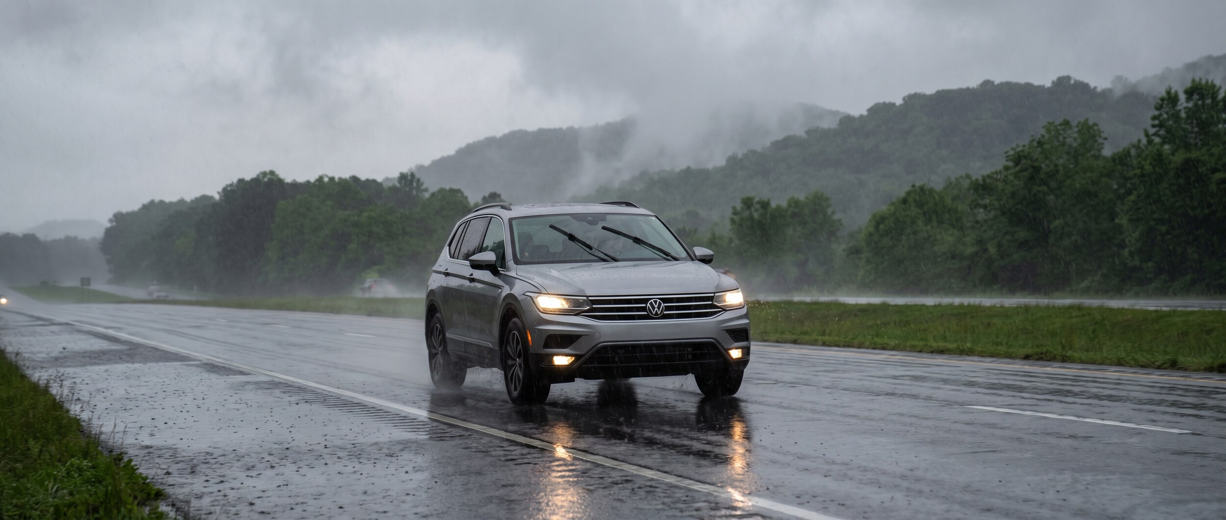 2026 Volkswagen Tiguan driving in heavy rain on a wet Upstate South Carolina highway with wipers on and headlights illuminated