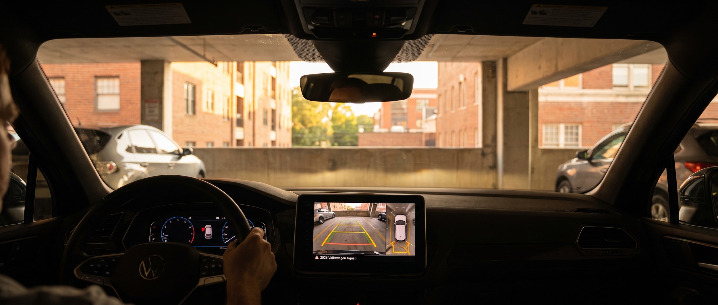 2026 Volkswagen Tiguan backing into a downtown Greenville parking garage at dusk with rearview camera display