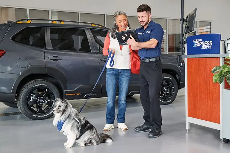 Service advisor reviewing vehicle service details with a customer and her dog at Subaru Express Service