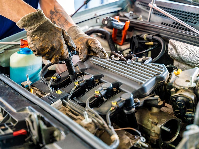 Mechanic in the process of replacing a spark plug on engine.