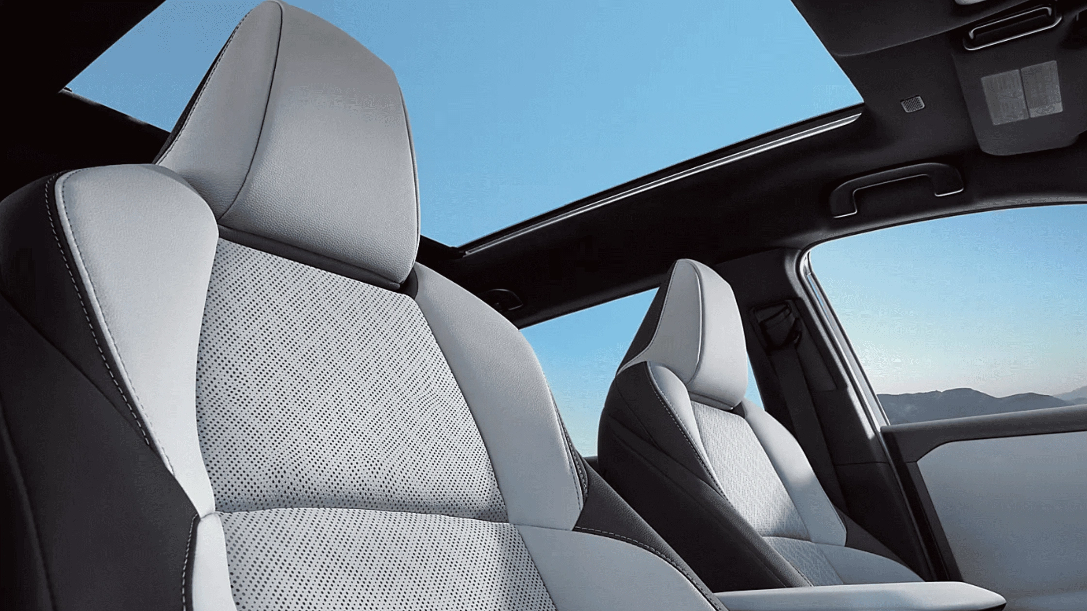 2026 Subaru Solterra electric SUV interior featuring grey perforated front seats and panoramic glass roof open to a clear blue sky