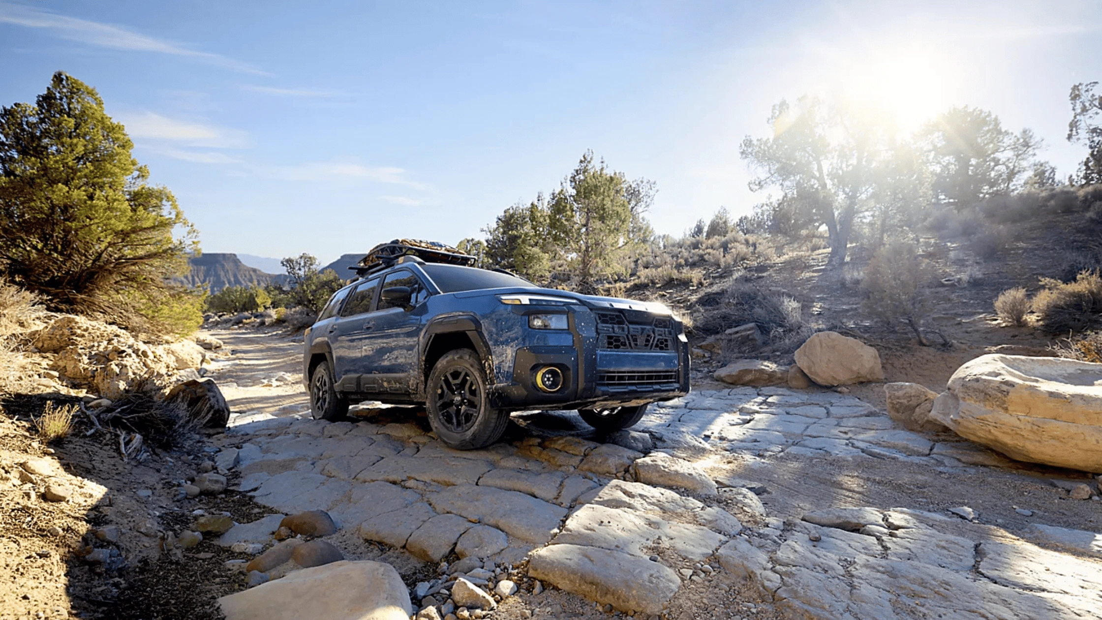 2026 Subaru Outback Wilderness in blue navigating a rocky off-road trail with roof rack in a desert canyon landscape, available in Pueblo CO