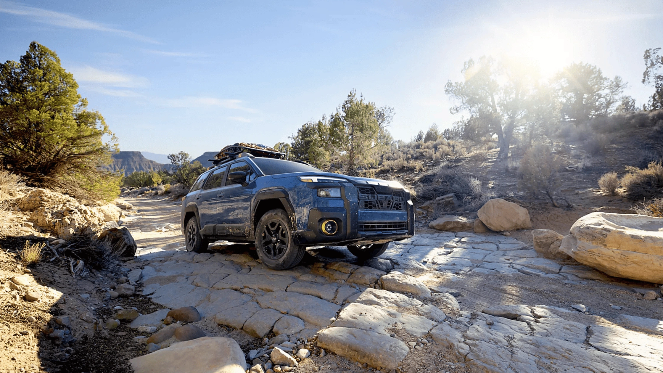 2026 Subaru Outback Wilderness in blue navigating a rocky off-road trail with roof rack in a desert canyon landscape, available in Pueblo CO