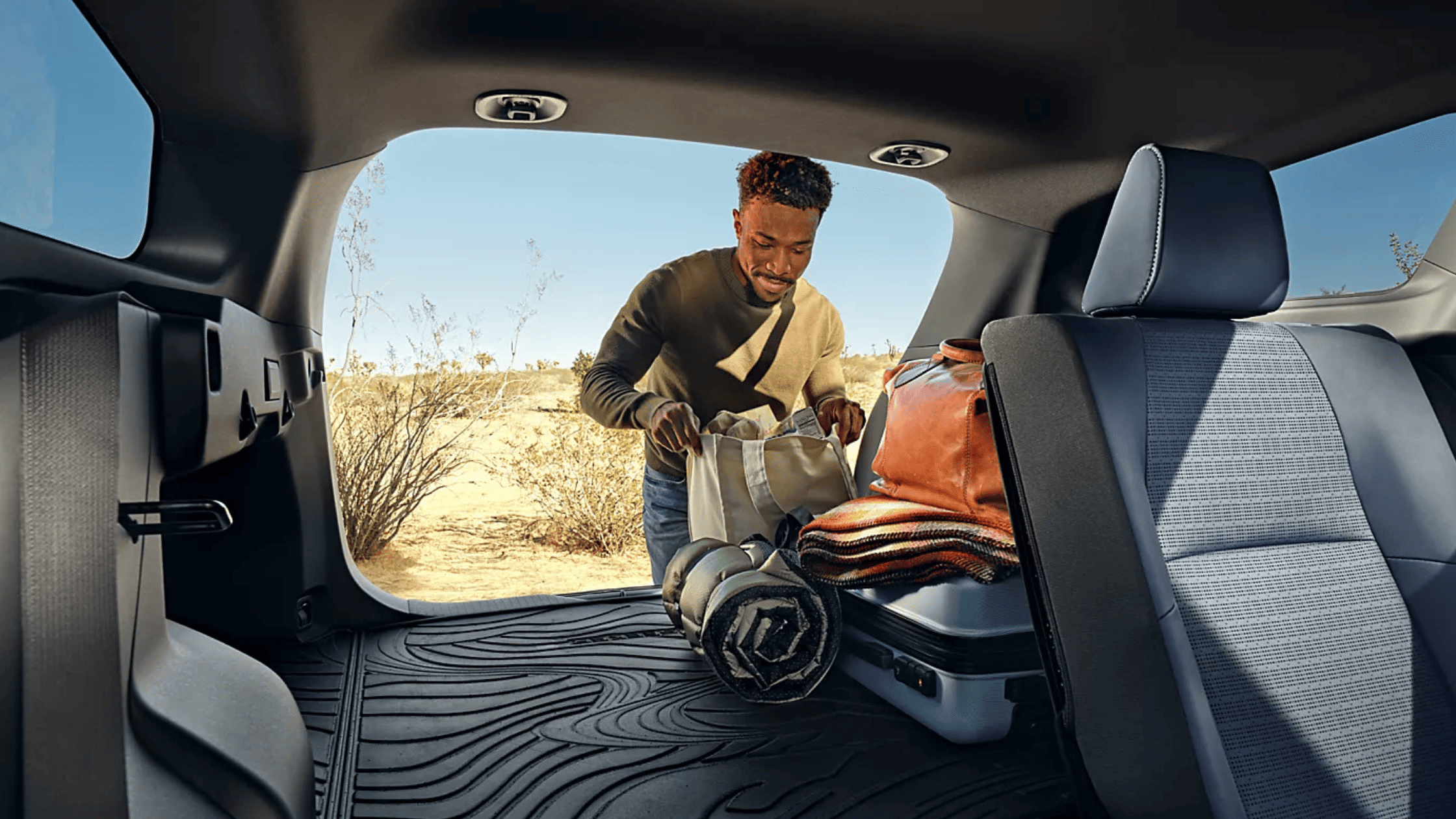 2026 Subaru Outback Wilderness cargo area loaded with camping gear including sleeping bag and trekking poles with rear hatch open in a desert setting
