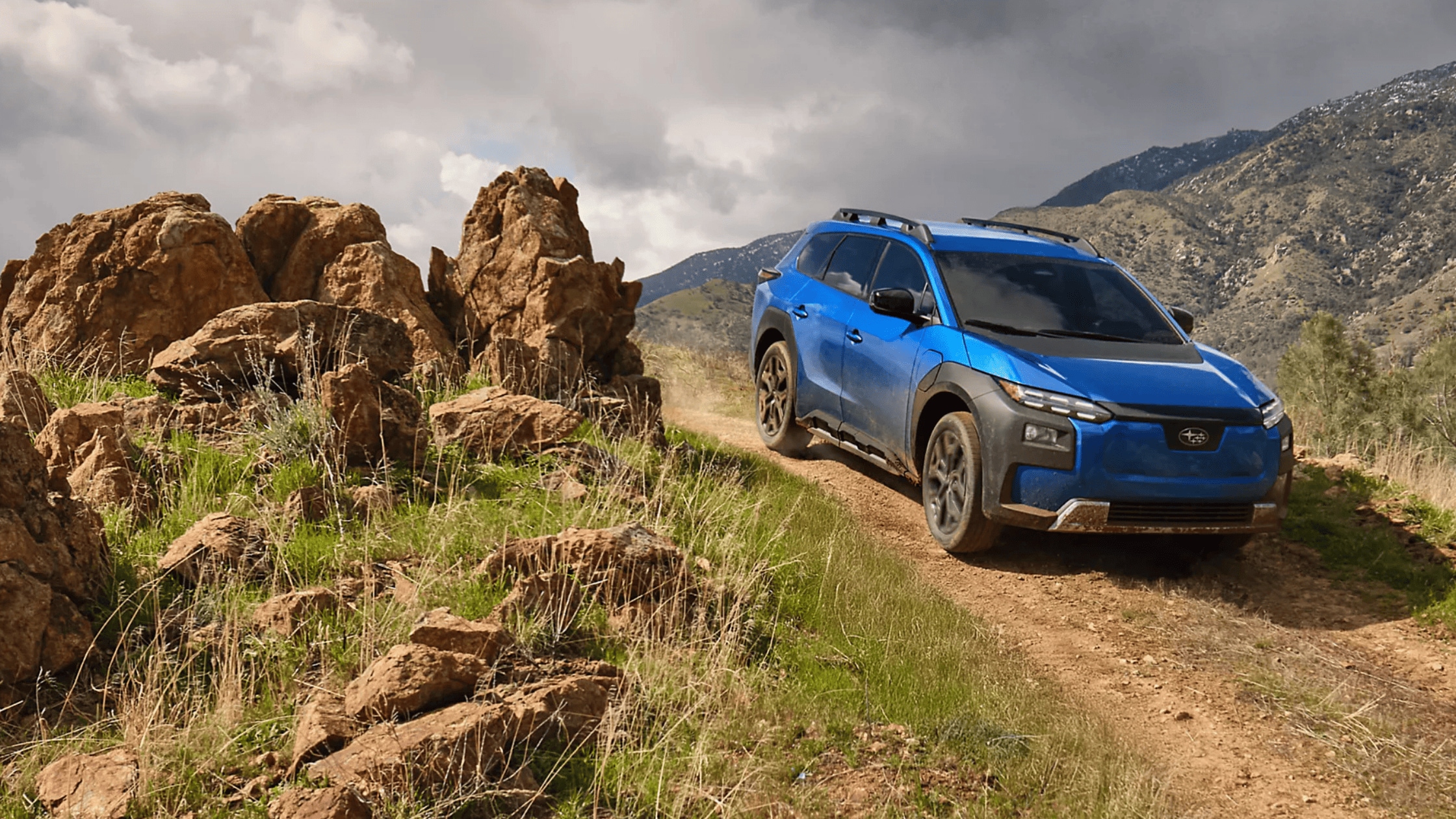 2026 Subaru Trailseeker electric SUV in blue with black cladding and roof rails navigating rocky mountain dirt trail in Colorado Springs CO